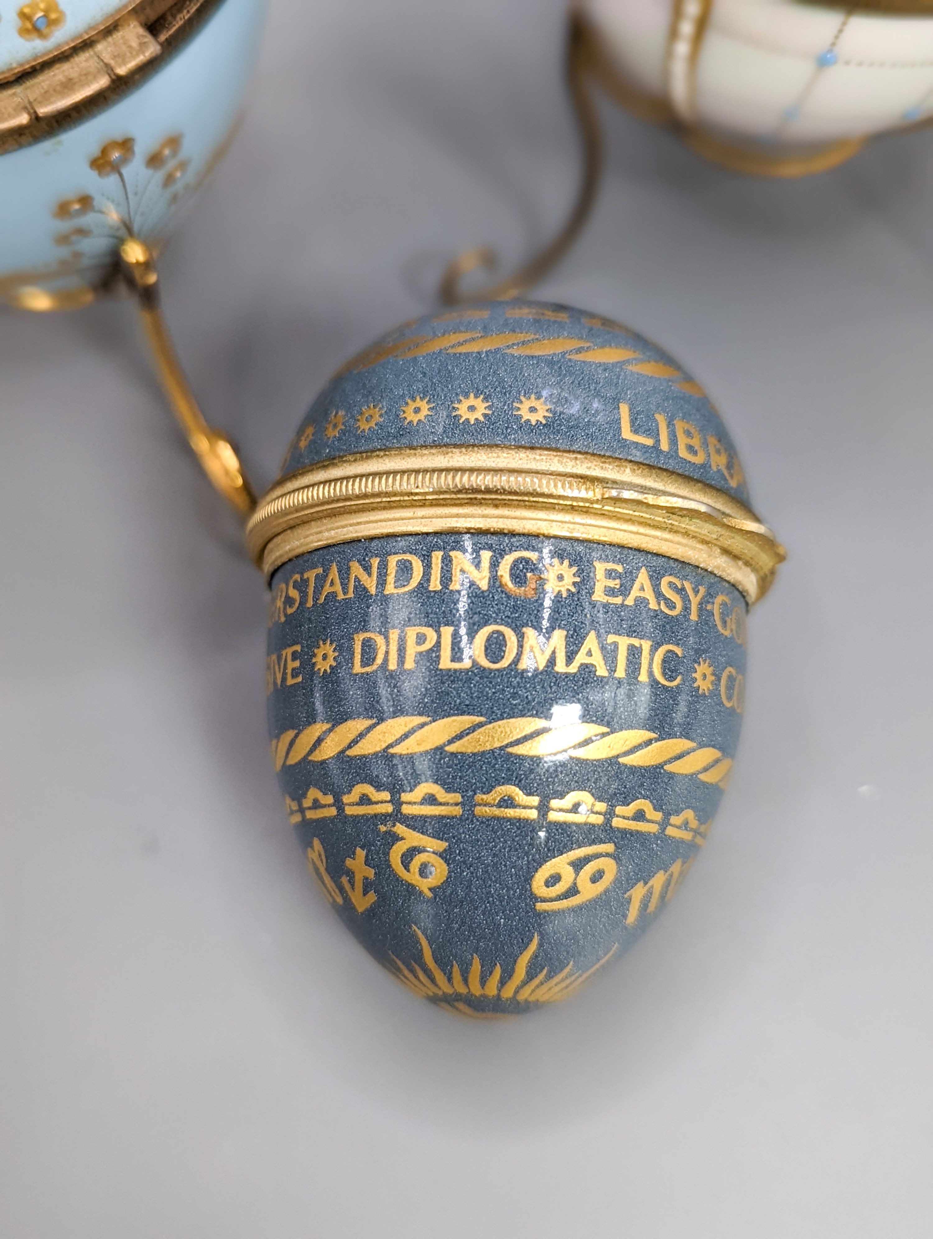 Two silver gilt mounted enamelled eggs with interior seascapes, on silver gilt stands, Birmingham, 1985 & 7 and a smaller similar gilt metal mounted zodiac egg, tallest 8.5cm